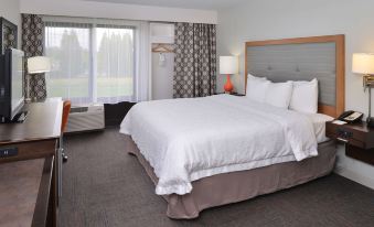 a large bed with white sheets and a wooden headboard is in a room with gray carpet at Hampton Inn Portland East