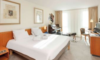 a large bed with white sheets and a headboard is in a room with beige carpeting at Novotel Freiburg am Konzerthaus