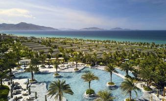 a resort with a large pool surrounded by palm trees and the ocean in the background at Movenpick Resort Cam Ranh