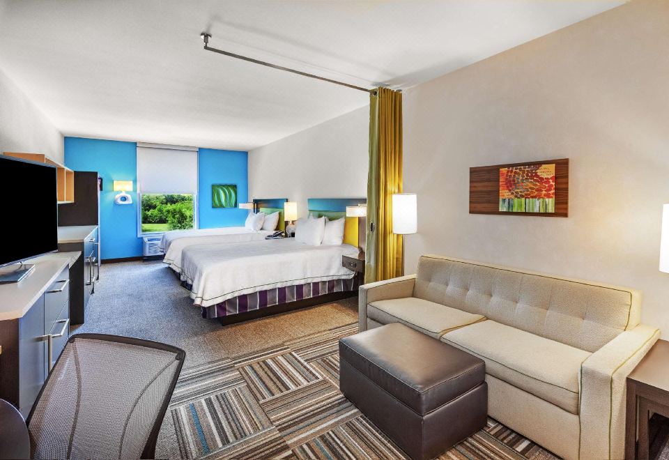 a modern hotel room with a bed , couch , and dining table , along with a tv and other amenities at Home2 Suites by Hilton Gonzales