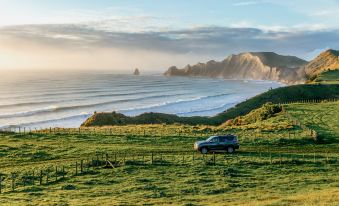 a black car is driving on a dirt road near a grassy field and the ocean at Rosewood Cape Kidnappers