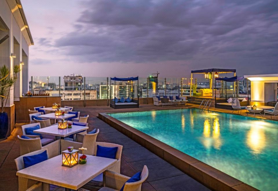 an outdoor pool surrounded by a rooftop deck , with tables and chairs placed around the pool for guests to enjoy at The Park Chennai