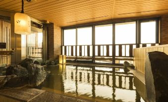 a large indoor pool with a wooden ceiling and walls , surrounded by windows that offer views of the outdoors at Dormy Inn Mishima