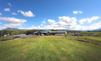 a large grassy field with a building in the background , surrounded by trees and hills at Hotel Eyjafjallajokull