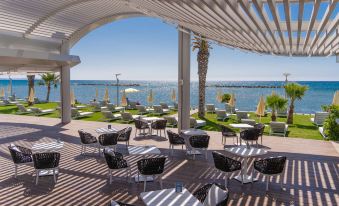 a patio area with black chairs and tables , an umbrella , and a view of the ocean at Radisson Beach Resort Larnaca
