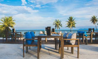 a wooden table with blue cushions and a laptop on it , surrounded by chairs , overlooking the ocean at Seanery Beach Resort