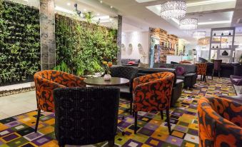 a modern , well - lit restaurant with green walls and black chairs , decorated with a large plant mural on the ceiling at Hotel Verde Cape Town Airport