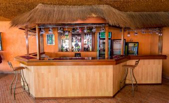 a wooden bar with a thatched roof , surrounded by various liquor bottles and glasses , under a thatched roof at Belvedere Hotel