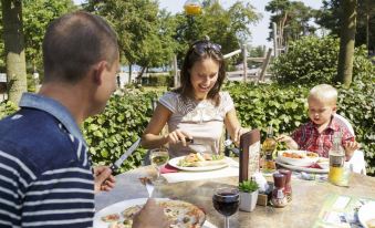 a group of people , including a man and a woman , are enjoying a meal together at an outdoor dining table in a park setting at Sunparks Kempense Meren