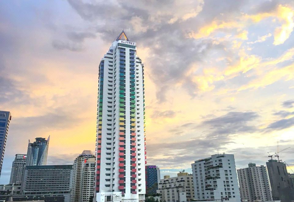 A tall building stands illuminated against a backdrop of a blue sky at dusk at Baiyoke Suite Hotel