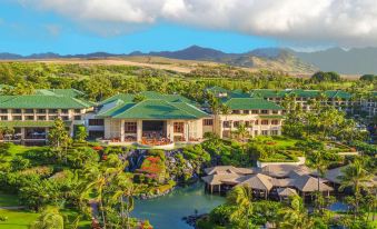 a large , multi - story building with a green roof is surrounded by lush greenery and mountains at Grand Hyatt Kauai Resort and Spa