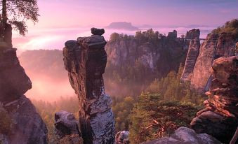 a picturesque view of a mountain with a large rock formation , surrounded by trees and fog at Berghotel Bastei