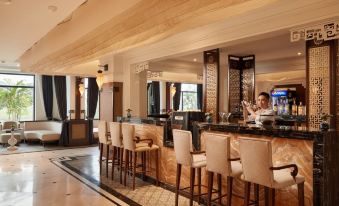a modern , elegant bar with marble floors and wooden furniture , surrounded by large windows and a man sitting at the counter at Ninh Binh Hidden Charm Hotel & Resort
