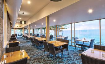 a restaurant with tables and chairs , a large window , and a view of the ocean at Aurora Ozone Hotel Kangaroo Island