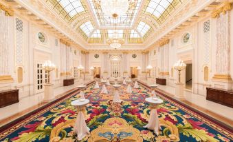 a grand hall with a long banquet table and colorful carpet , surrounded by white walls and large windows at Fairmont Grand Hotel - Kyiv