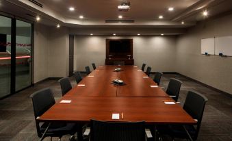 a long wooden conference table with black chairs , set up for a meeting in an empty room at Aloft Coral Gables