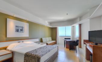 a modern hotel room with a large bed , desk , and couch , as well as a balcony overlooking the ocean at Grand Mercure Recife Boa Viagem