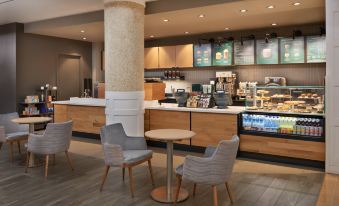 a modern coffee shop with wooden tables and chairs , a tall pillar , and various coffee makers at Sheraton Parkway Toronto North Hotel & Suites