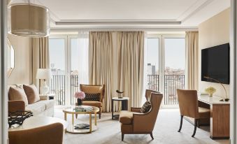 a luxurious hotel room with beige curtains , wooden furniture , and a balcony offering views of the city at Four Seasons Hotel Madrid