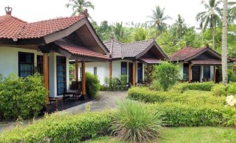a row of wooden houses with a red tile roof , surrounded by greenery and bushes at Tasik Ria Resort