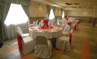 a well - decorated banquet hall with multiple round tables covered in white tablecloths and adorned with red napkins at Hotel Ritz