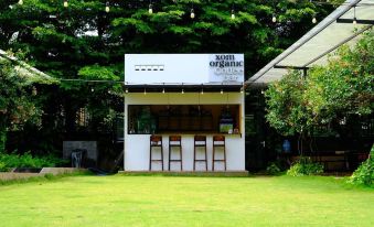 a white building with a bar and stools is situated in a grassy area , surrounded by trees at XOM Organic Farm Stay