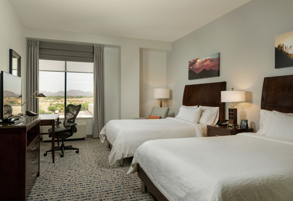 a hotel room with two beds , a desk , and a large window overlooking the city at Hilton Garden Inn Phoenix Airport North