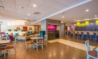 a modern hotel lobby with a reception desk , dining area , and seating area , all decorated in warm colors at Home2 Suites by Hilton Lake City