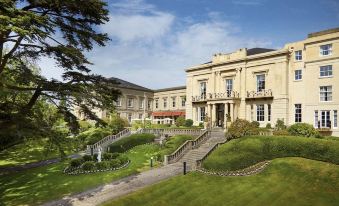 a large , elegant mansion with a staircase leading up to the entrance , surrounded by lush greenery at Macdonald Bath Spa Hotel