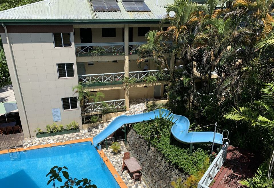 a hotel with a swimming pool and a water slide , surrounded by lush greenery and trees at Suva Motor Inn