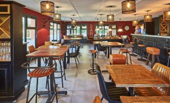 a large , empty restaurant with wooden tables and chairs , set against a red wall with hanging lights at Kyriad Lille Est - Hem