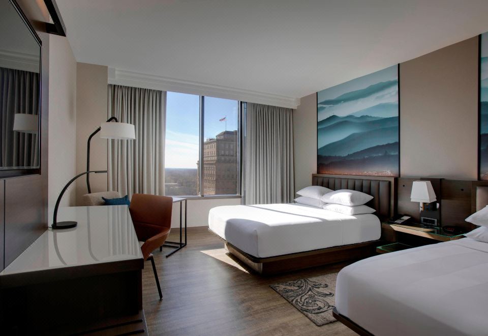 a modern hotel room with two beds , a desk , and a large window overlooking the city at Winston-Salem Marriott