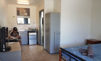 a small kitchen with a refrigerator , a sink , and a dining table in the background at Coolgardie GoldRush Motels