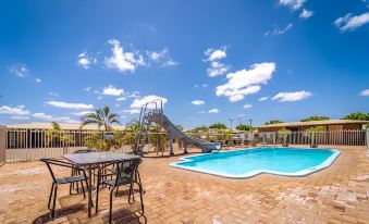 a sunny day at an outdoor pool area with a swimming pool , dining table , chairs , and a slide at Carnarvon Motel
