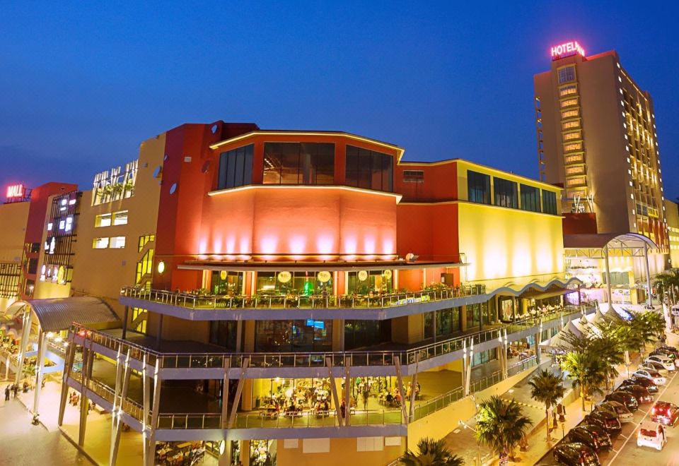 a colorful building with a restaurant and several shops is illuminated at night , surrounded by palm trees at Palm Seremban Hotel