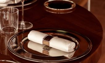 a dining table with a wine glass , wine bottle , and a napkin on a silver plate at Cap d'Antibes Beach Hotel