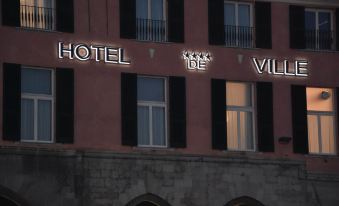 "a red building with black shutters , and the sign "" hotel "" is lit up above it" at Hotel de Ville
