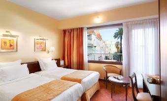 a hotel room with two beds , a window , and a chair near the window , all decorated in warm colors at Splendid Hotel & Spa Nice