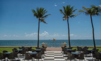 a beach scene with palm trees , a checkered floor , and several tables and chairs set up for dining at Galle Face Hotel