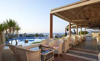 a beachside resort with a pool surrounded by chairs and tables , providing a comfortable outdoor dining area at Aldemar Knossos Royal