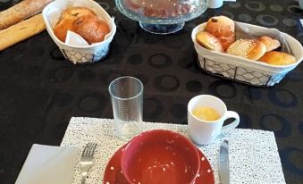 a table is set with a red bowl , glass of orange juice , bread basket , and silverware at La Bastide