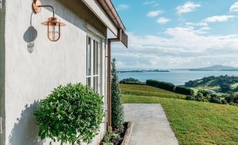 a white building with a balcony and greenery , overlooking a scenic view of the ocean and hills at Mudbrick Cottages