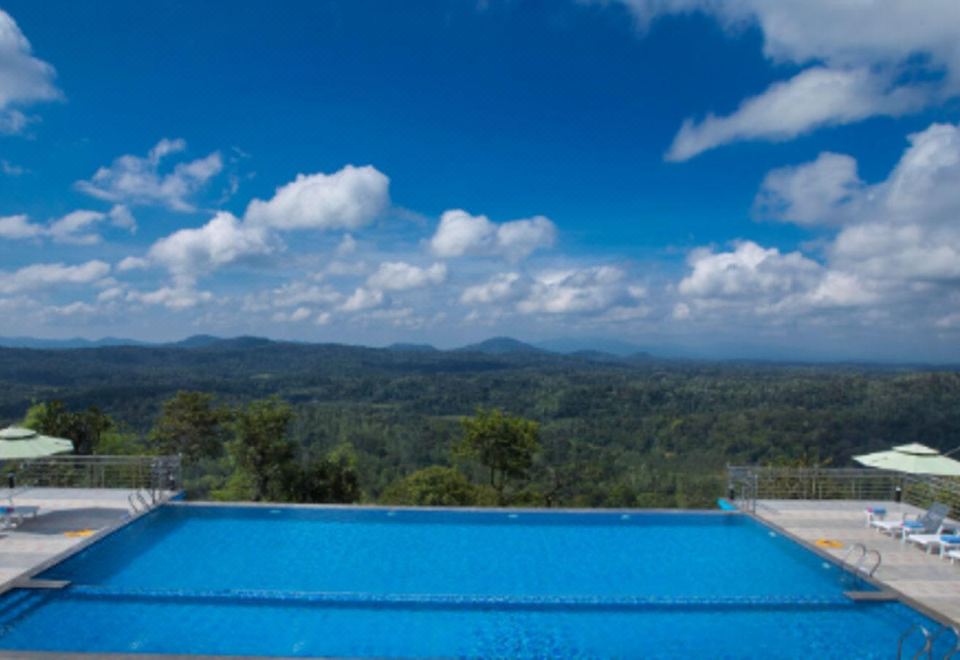 a large swimming pool with a view of the mountains in the background under a blue sky at Coorg Cliffs Resort