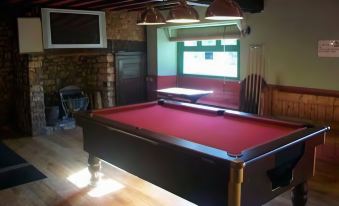 a billiards table with red felt , surrounded by wooden walls and hanging lights , in a room with a window and a stone fireplace at The Seven Stars