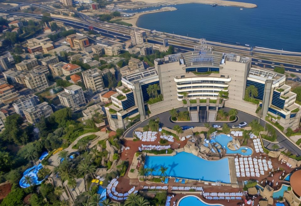 an aerial view of a large hotel with a pool surrounded by palm trees and water at Le Royal Hotel - Beirut