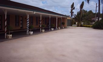 a row of buildings with a pink floor and palm trees in the background , under a cloudy sky at Ballina Colonial Motel