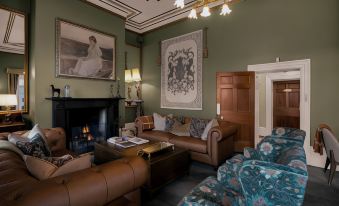 a cozy living room with brown leather couches , a fireplace , and green walls , decorated with paintings and artwork at Quamby Estate