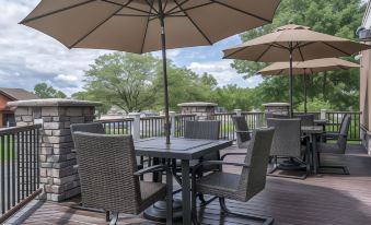 a wooden deck with a table , chairs , and umbrellas for outdoor dining , surrounded by trees and a body of water at Ramada by Wyndham Minneapolis Golden Valley