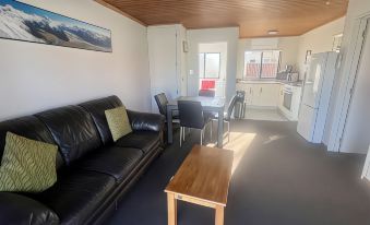 a living room with a black leather couch , wooden coffee table , and kitchen in the background at Pinewood Motels