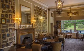 a dining room with a fireplace , tables and chairs , and a chandelier hanging from the ceiling at Banchory Lodge Hotel